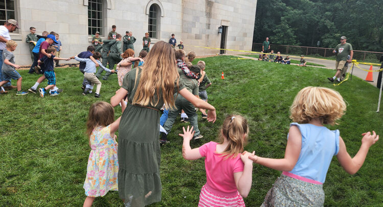 A scattered group of families with their children running and playing games in the grass.