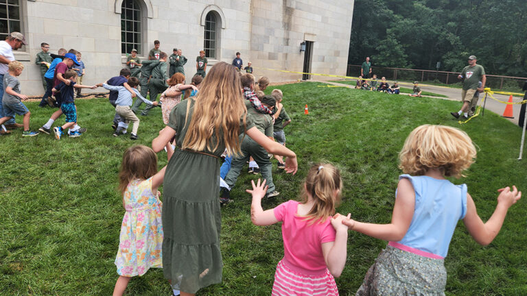 A scattered group of families with their children running and playing games in the grass.