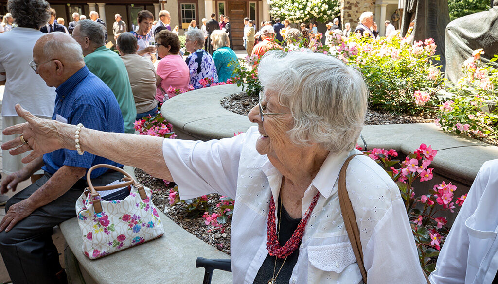 An elderly woman enjoying the festivities of the Celebration of Rosa, with many others, outside in the Shrine's court.