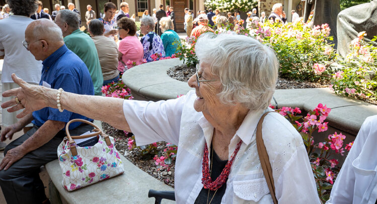 An elderly woman enjoying the festivities of the Celebration of Rosa, with many others, outside in the Shrine's court.