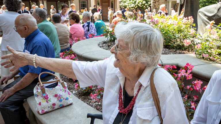 An elderly woman enjoying the festivities of the Celebration of Rosa, with many others, outside in the Shrine's court.