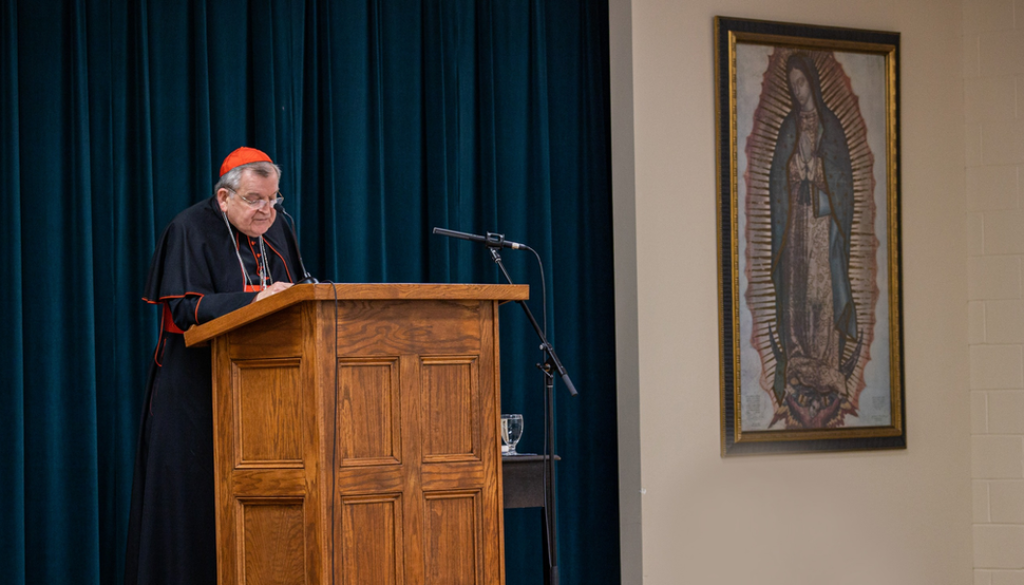 Cardinal Burke speaking at a podium during the Queen of the Americas Guild Conference. Our Lady of Guadalupe Shrine, La Crosse, Wisconsin.