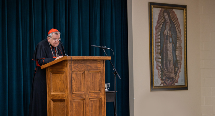 Cardinal Burke speaking at a podium during the Queen of the Americas Guild Conference. Our Lady of Guadalupe Shrine, La Crosse, Wisconsin.