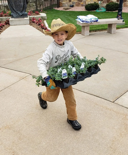 A child holding a tray of flowers on the grounds of Our Lady of Guadalupe Shrine in La Crosse, Wisconsin.