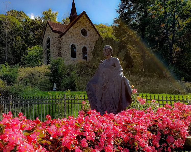 Statue of Juan Diego surrounded by flowers in the garden of Our Lady of Guadalupe Shrine in La Crosse, Wisconsin.