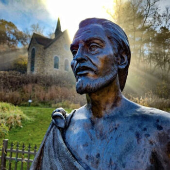 Close up of the statue of Juan Diego with the sun illuminating the votive candle chapel in the background at Our Lady of Guadalupe Shrine in La Crosse, Wisconsin.