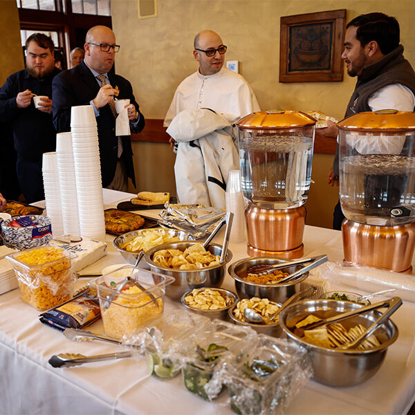 A small group of people near a table of chili toppings while enjoying a cup of chili.