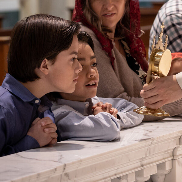 A closeup of two young boys admiring a relic held by a priest at the Shrine Church.