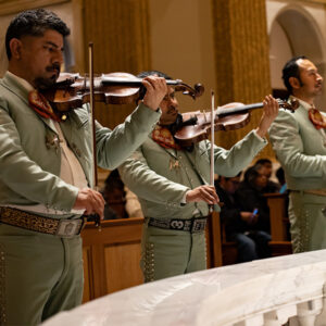 Closeups of two musicians playing in the mariachi band playing violins.