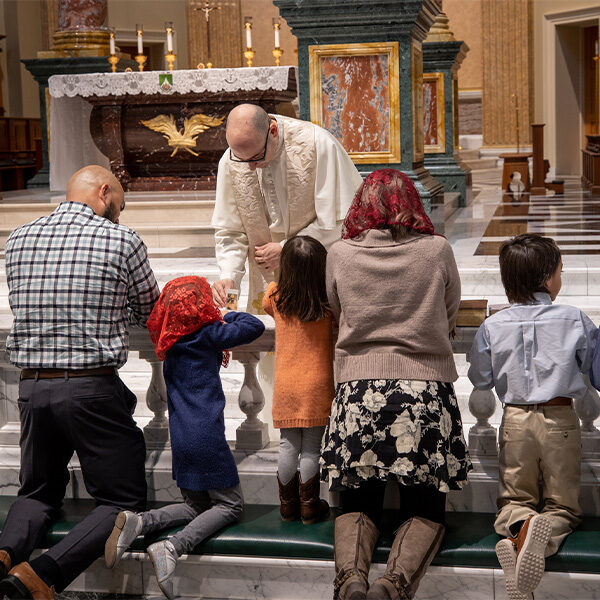 A Norbertine Priest in the Shrine Church holds a relic for the Morales Family to venerate as they kneel at the communion rail and ask for healing.