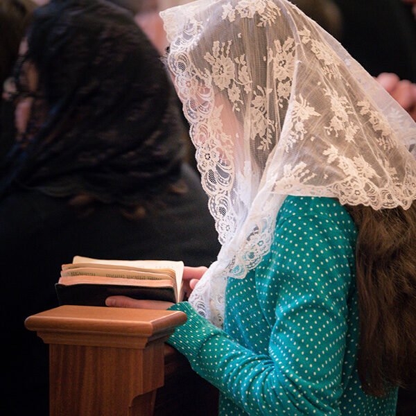 A woman praying in a pew at the Shrine church while wearing a lacy floral veil.