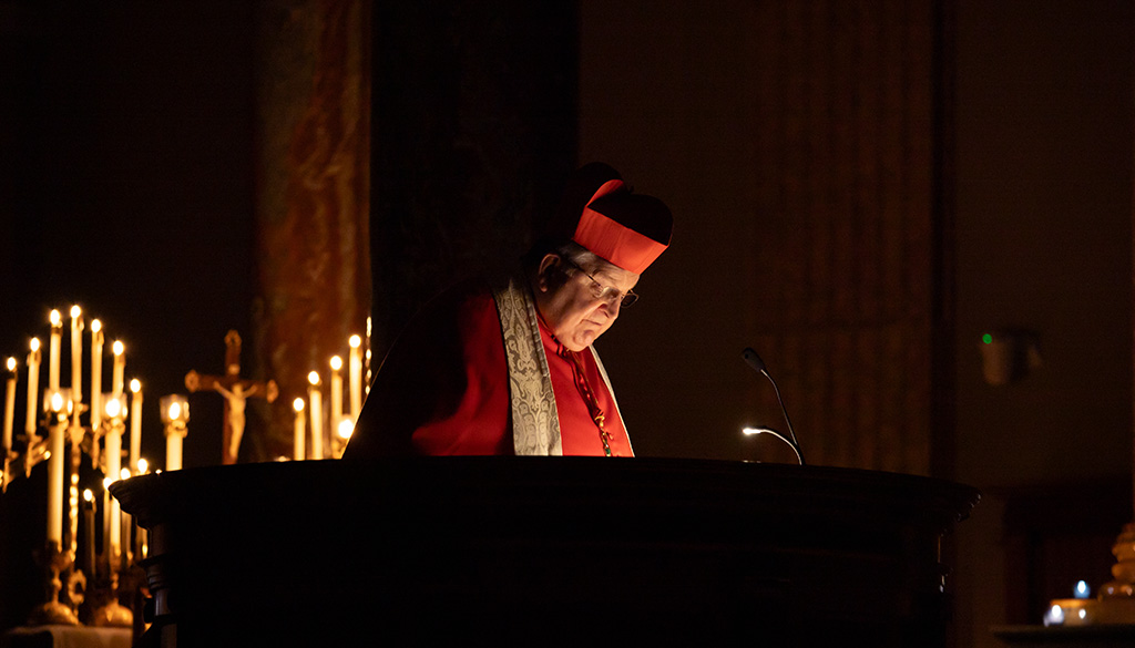 A candle-lit shot of Cardinal Burke focusing on his readings.