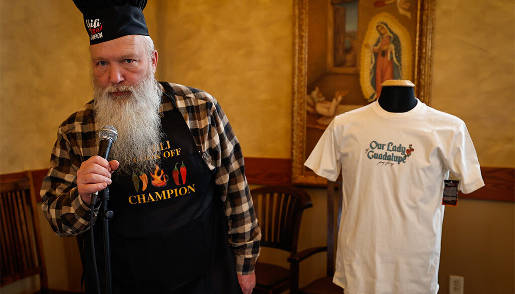 Chili cookoff winner, Deacon Sam wears his winning apron and prepares to speak into a microphone.