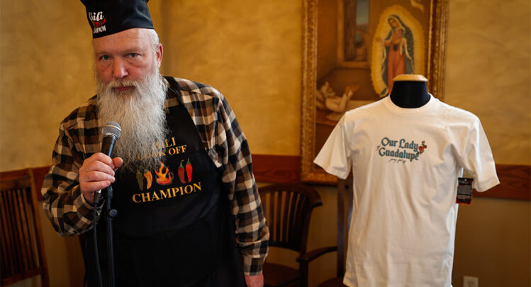 Chili cookoff winner, Deacon Sam wears his winning apron and prepares to speak into a microphone.