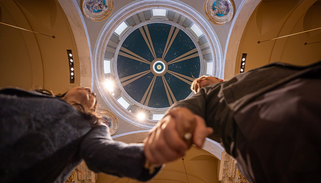 A worm's eye view of a newlywed couple holding hands under the blue church dome at the Shrine.