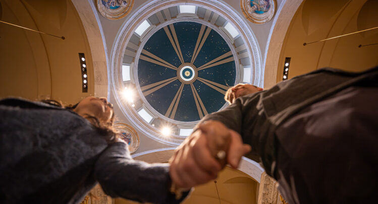 A worm's eye view of a newlywed couple holding hands under the blue church dome at the Shrine.