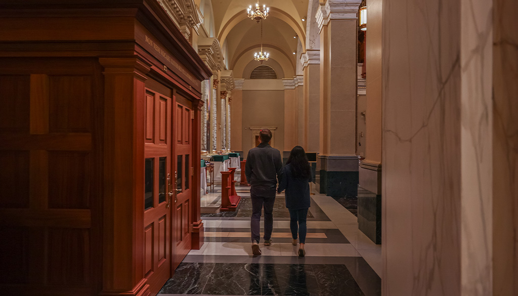 A newlywed couple holding hands while walking past the confessional area of the Shrine Church in La Crosse, Wisconsin.