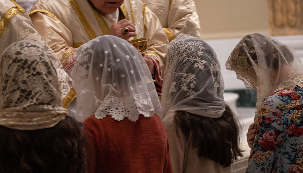 Four women wearing lacy floral veils while kneeling in from of Cardinal Burke during communion.