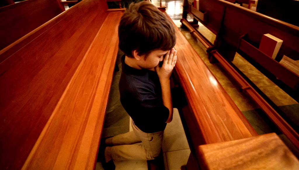 A young boy kneeled in the Shrine Church's pew, praying.