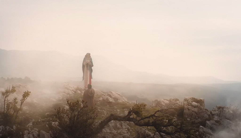 A serene misty landscape with a figure kneeling before the Shrine of Our Lady Guadalupe, set atop a rocky terrain in La Crosse, Wisconsin.